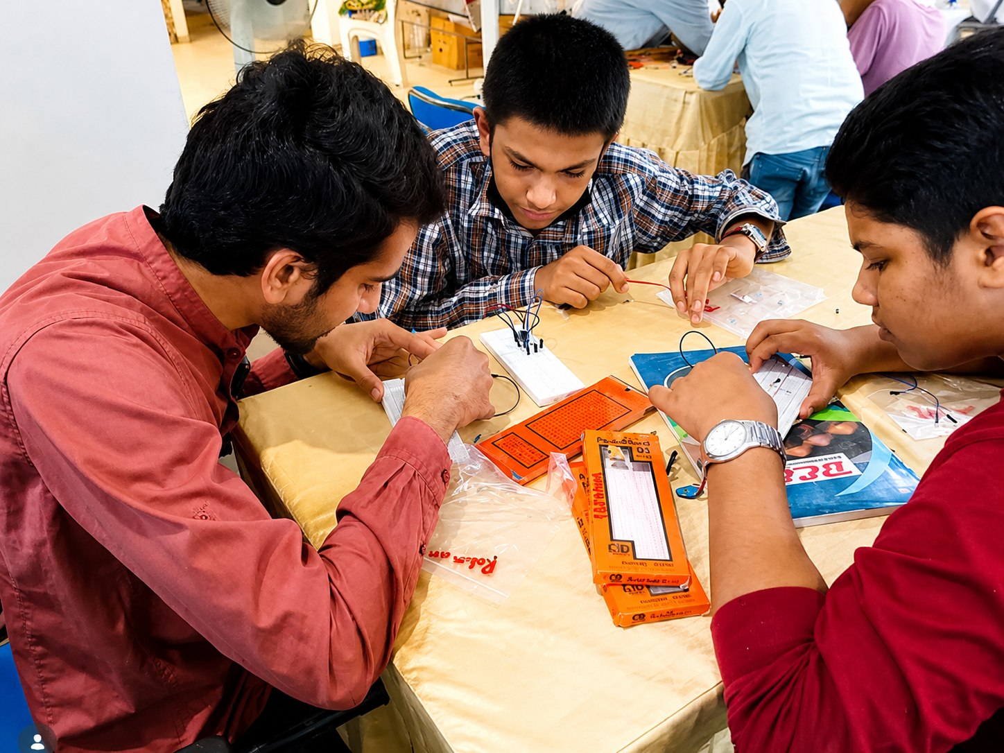 An instructor guiding two students as they assemble circuits on breadboards